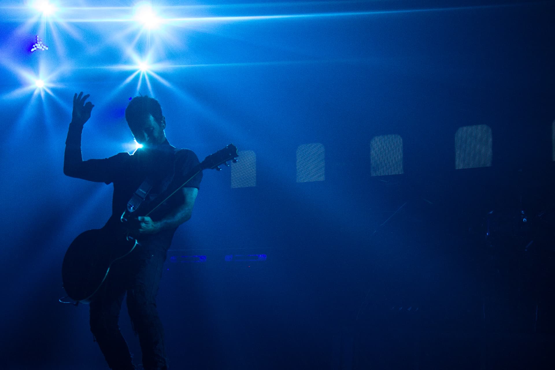 Guitarist silhouetted mid-strum against blue starburst stage lights
