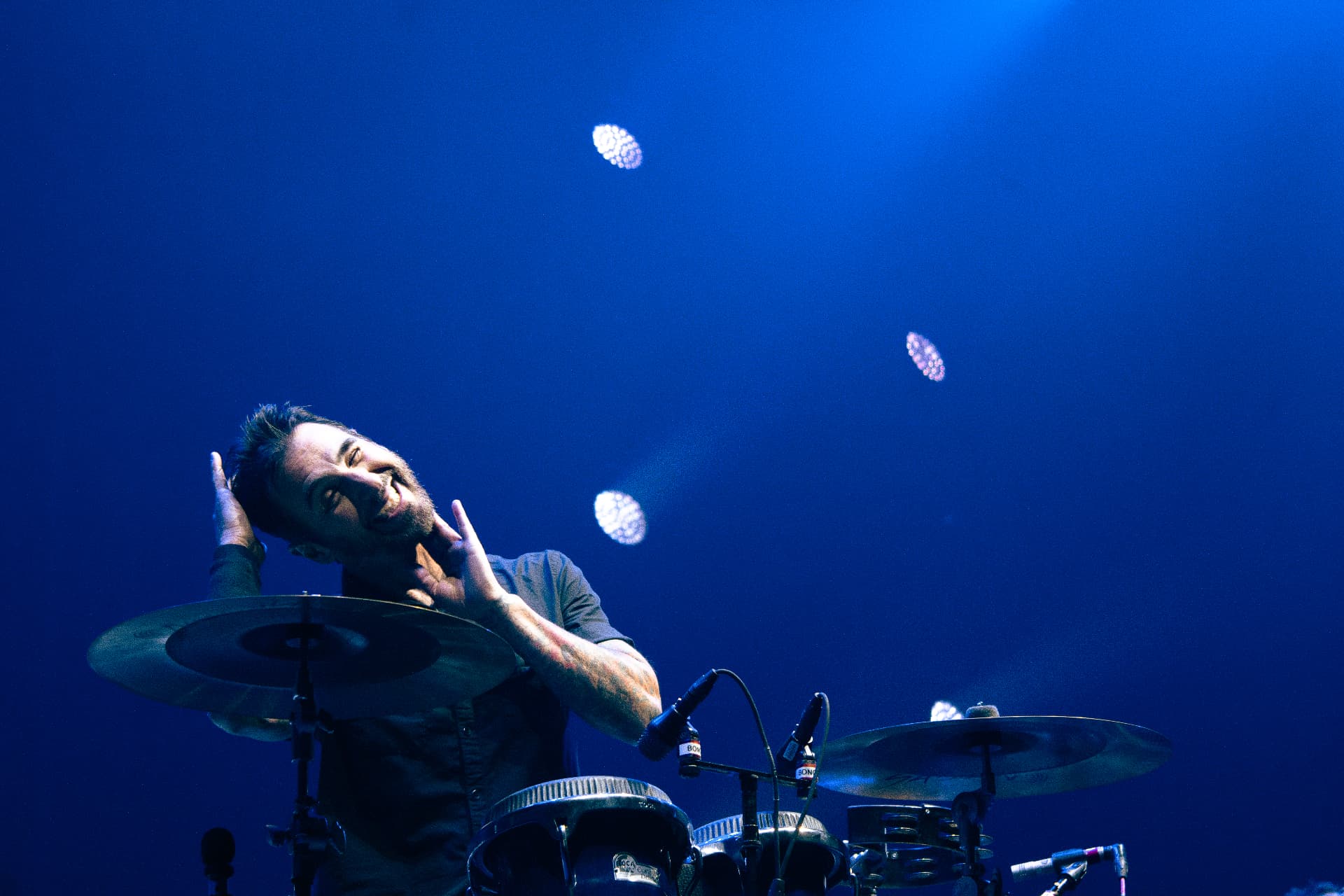 Drummer behind cymbals lit by deep blue stage light