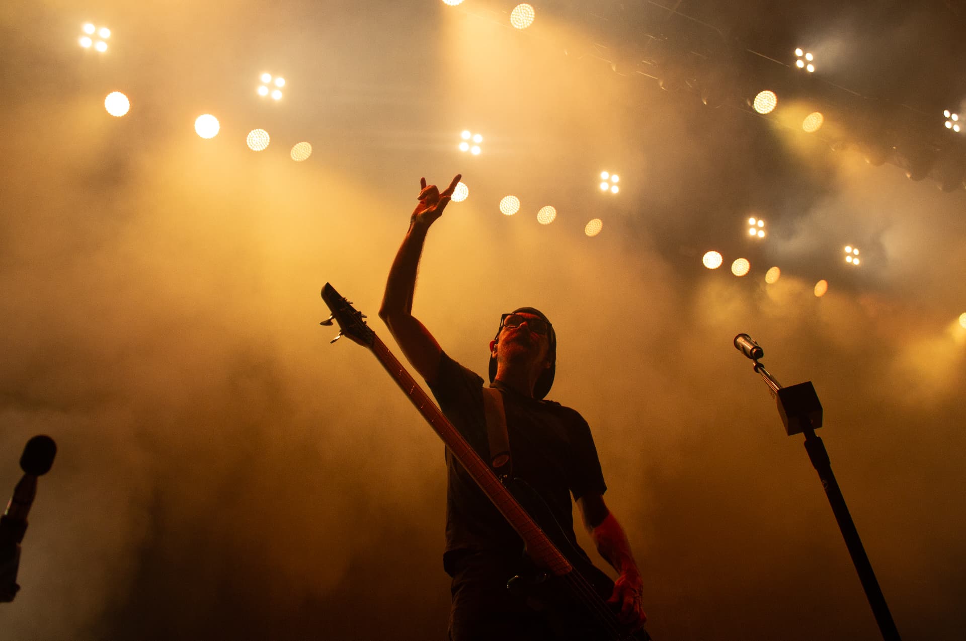 Bassist raising a hand into amber stage haze and backlight